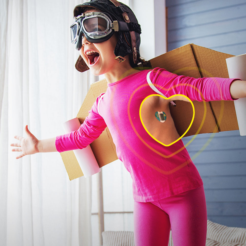 Child wearing a TraxIt wearable underarm thermometer while playing in a pink outfit